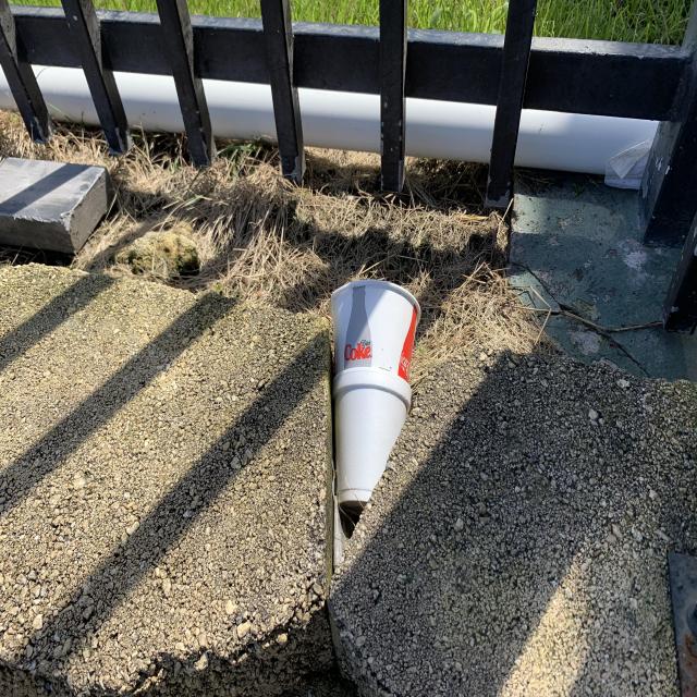A discarded cup beside a fence and pavement